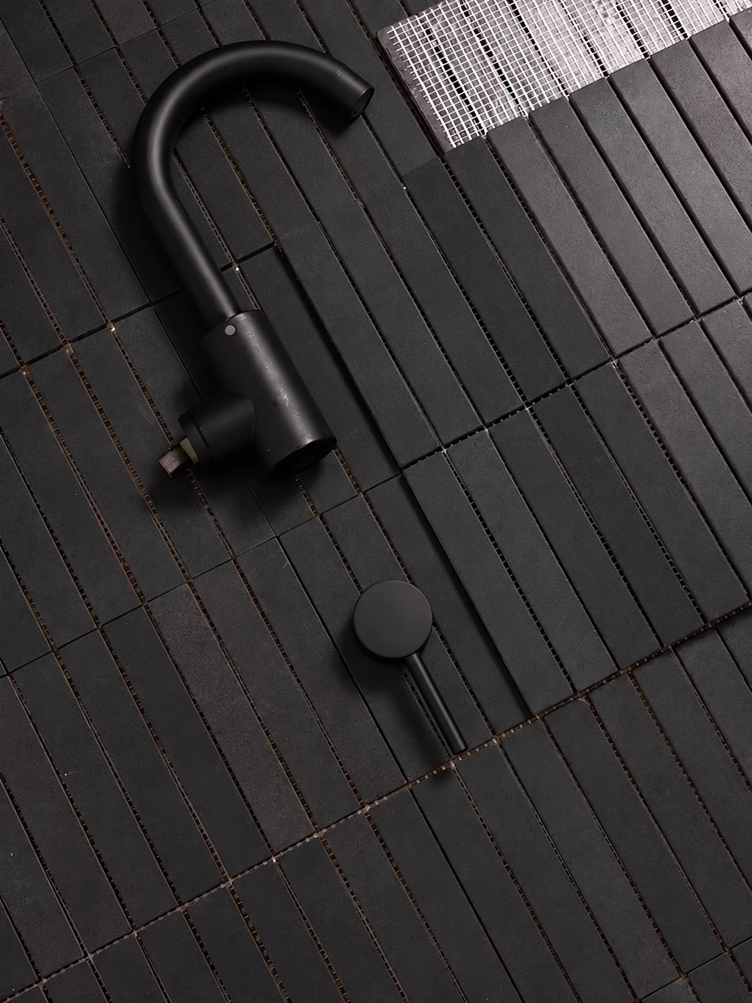 A matte black outdoor faucet with a matching round control knob, shown from an overhead angle on dark textured paving stones.