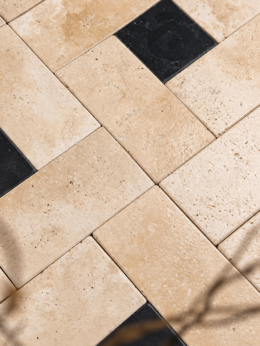 Natural beige travertine rectangular floor tiles arranged in a herringbone pattern with alternating black square accent tiles.