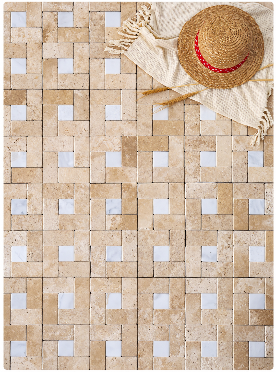 A rectangular mosaic tile sheet featuring a woven basketweave pattern of beige travertine and white marble tiles, styled with a straw hat and a cream fringed cloth in the top right corner.