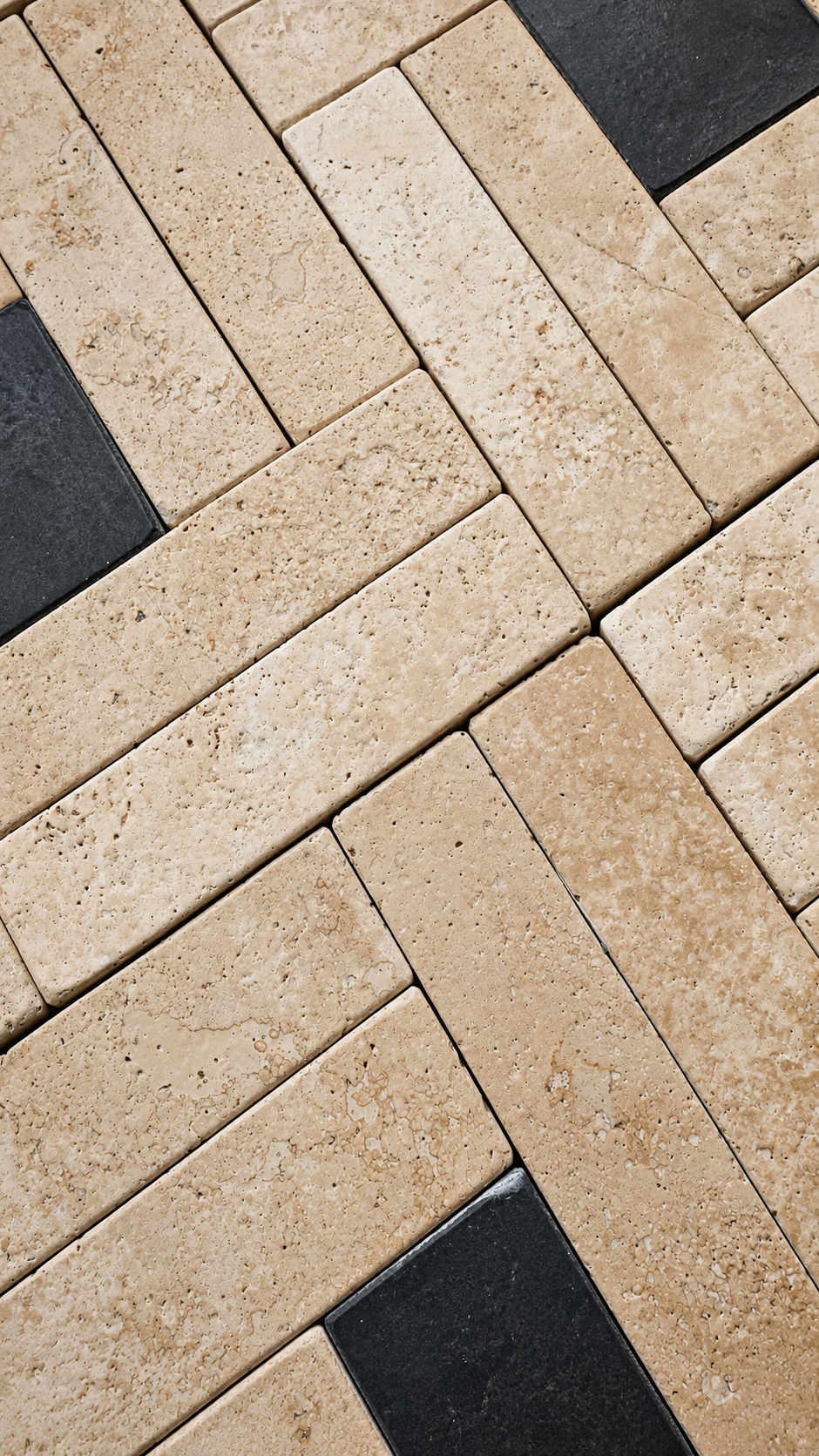 Natural beige travertine rectangular tiles arranged in a herringbone pattern, interspersed with dark charcoal gray accent tiles.