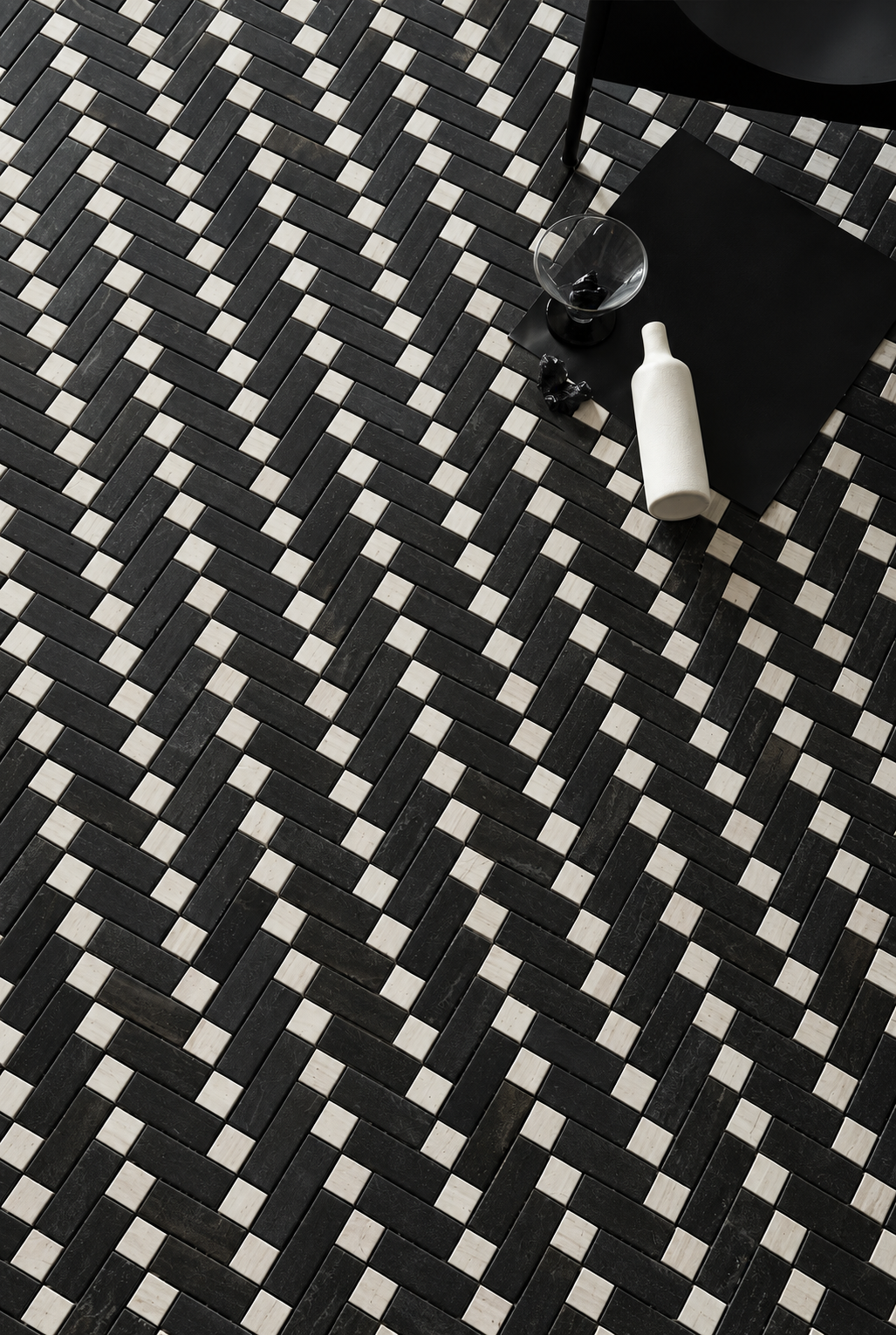 Black and white geometric patterned floor tiles arranged in a herringbone design, styled with a black chair, a glass, and a white bottle in the upper right corner.
