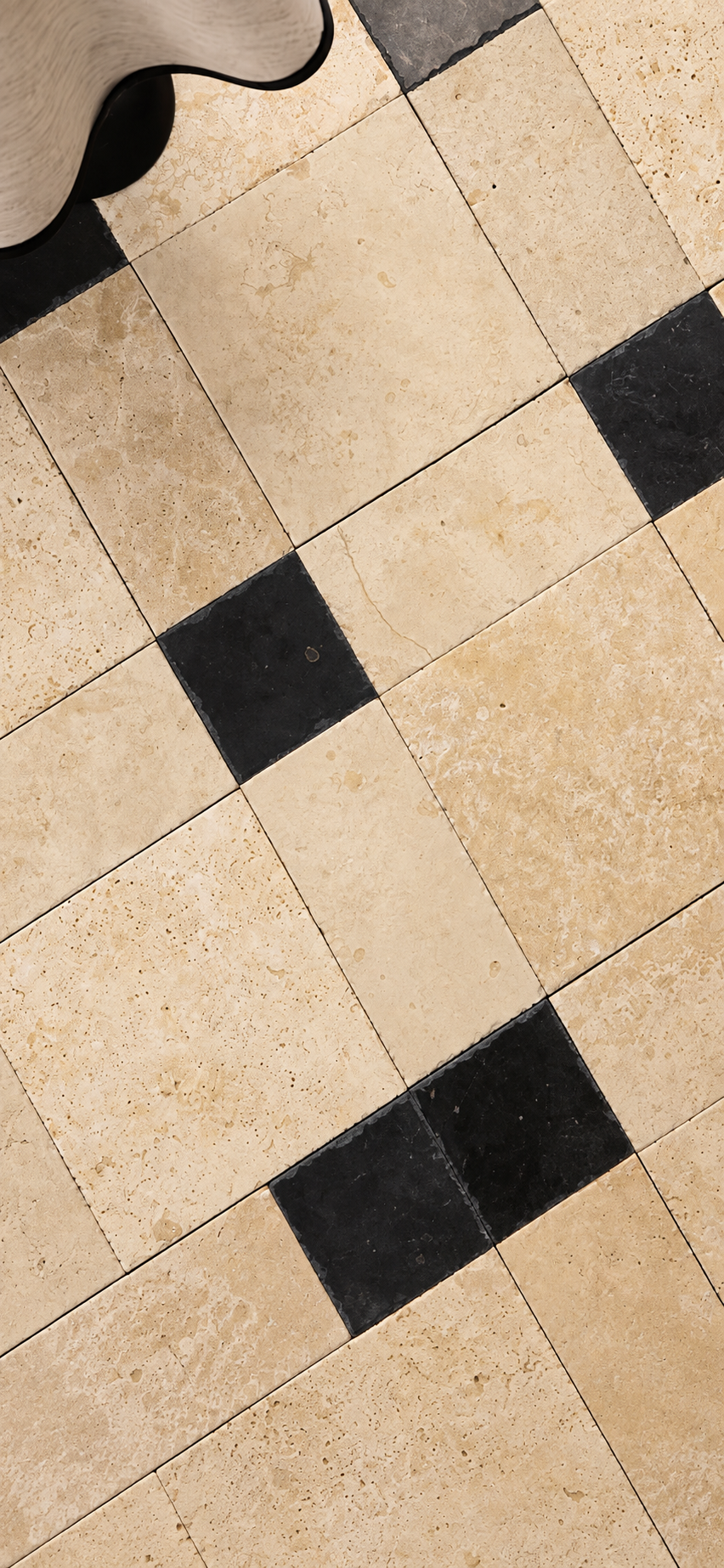 Beige travertine-style floor tiles arranged in a pattern with alternating black square tiles, shown from a top-down perspective.
