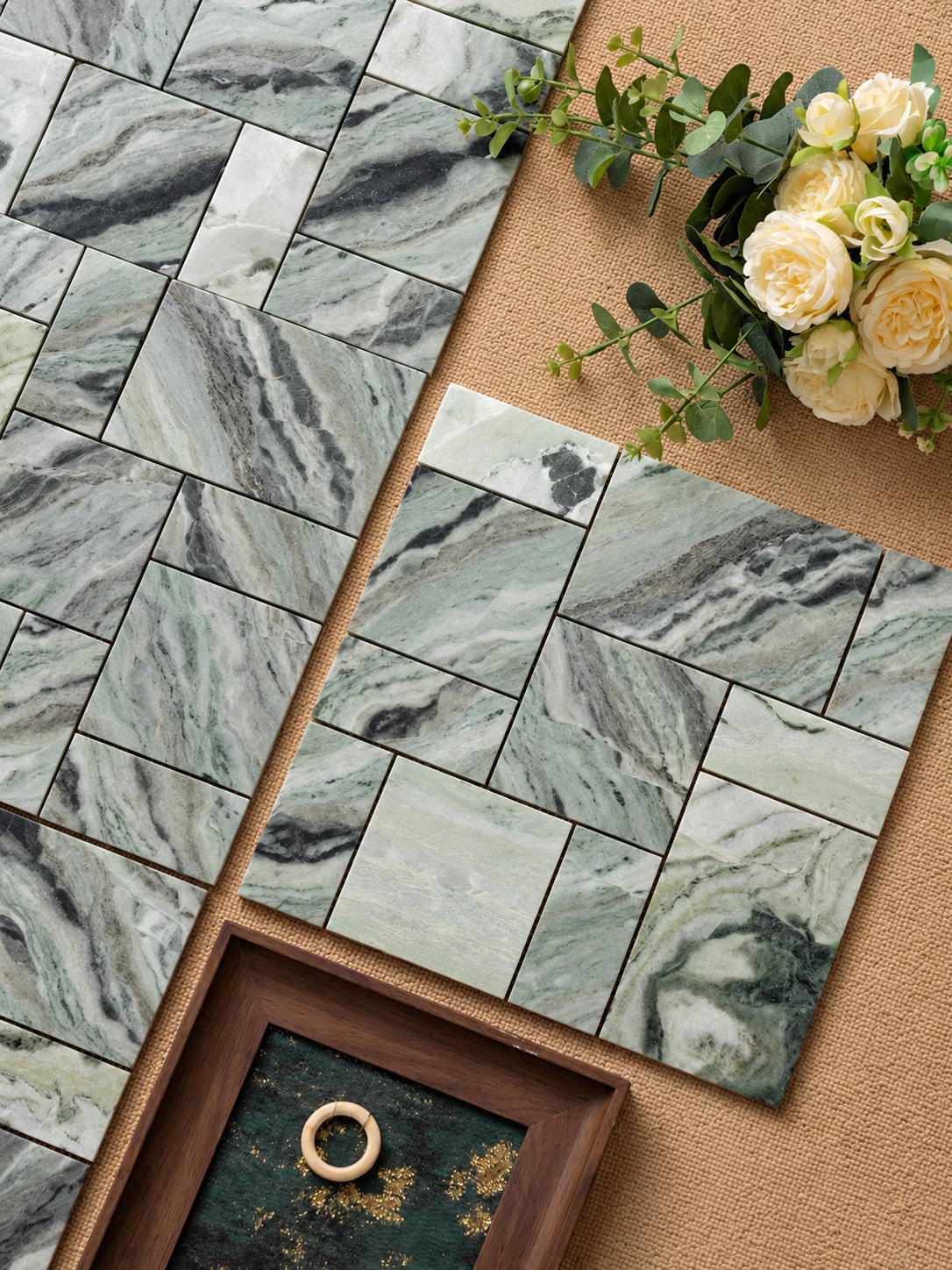 Green marble-look rectangular wall tiles arranged in a herringbone pattern, styled with cream roses, greenery, and a wooden tray on a tan textured background.