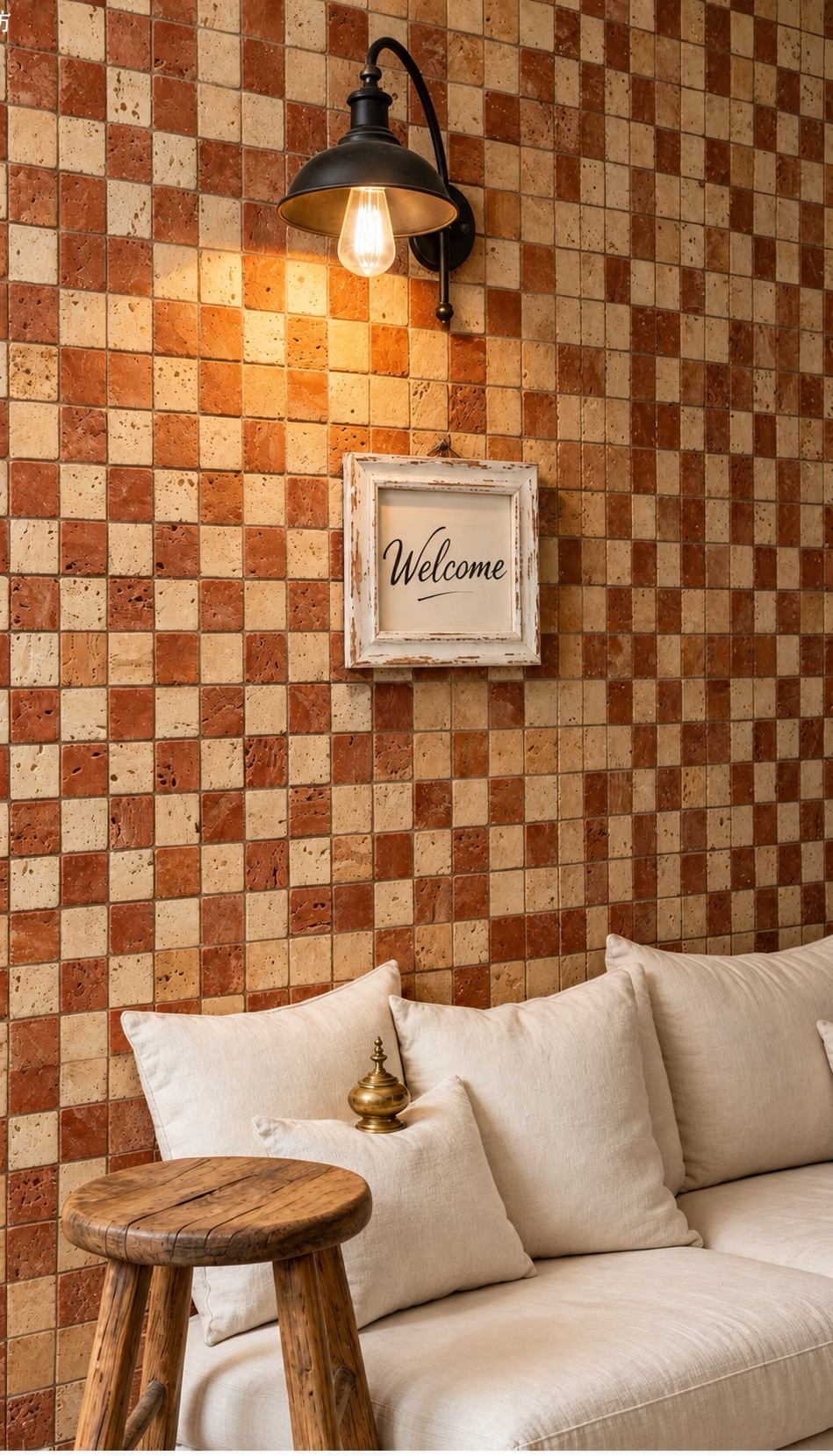 A cozy interior scene with a checkered wall made of warm brown and beige tiles, a black wall sconce with a glowing bulb, a small framed 'Welcome' sign, and a cream-colored sofa with pillows in the foreground.