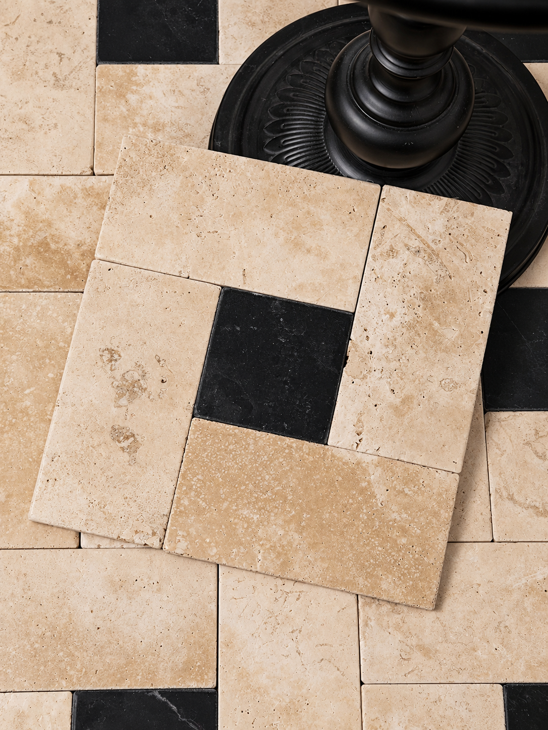 Beige travertine-style rectangular floor tiles arranged in a pattern with one central black tile, shown on a matching tile floor with a dark pedestal visible in the upper right.