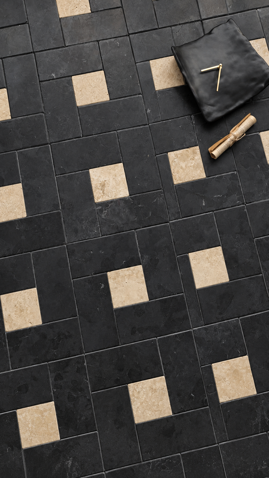 Black and beige geometric patterned floor tiles with a black fabric sample and a rolled gold sample on a dark surface.
