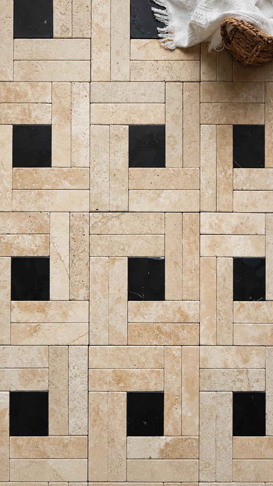 Beige travertine tile mosaic with a basketweave pattern and black square accents, styled with a white fringed cloth and a woven basket in the top right corner.