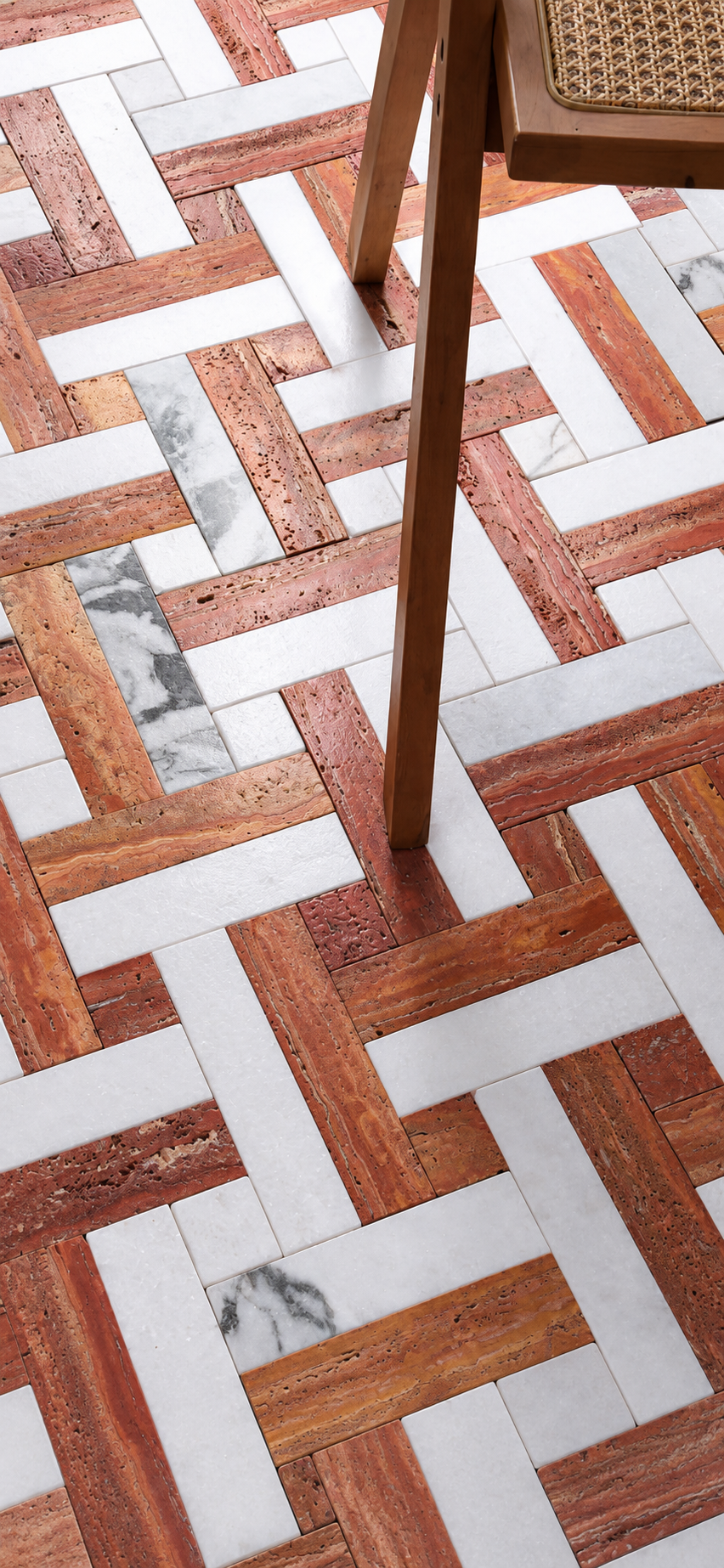 A close-up of a geometric mosaic floor made of reddish-brown wood planks, white stone tiles, and a few white marble veined accents. The legs of a wooden chair are visible in the upper right corner.