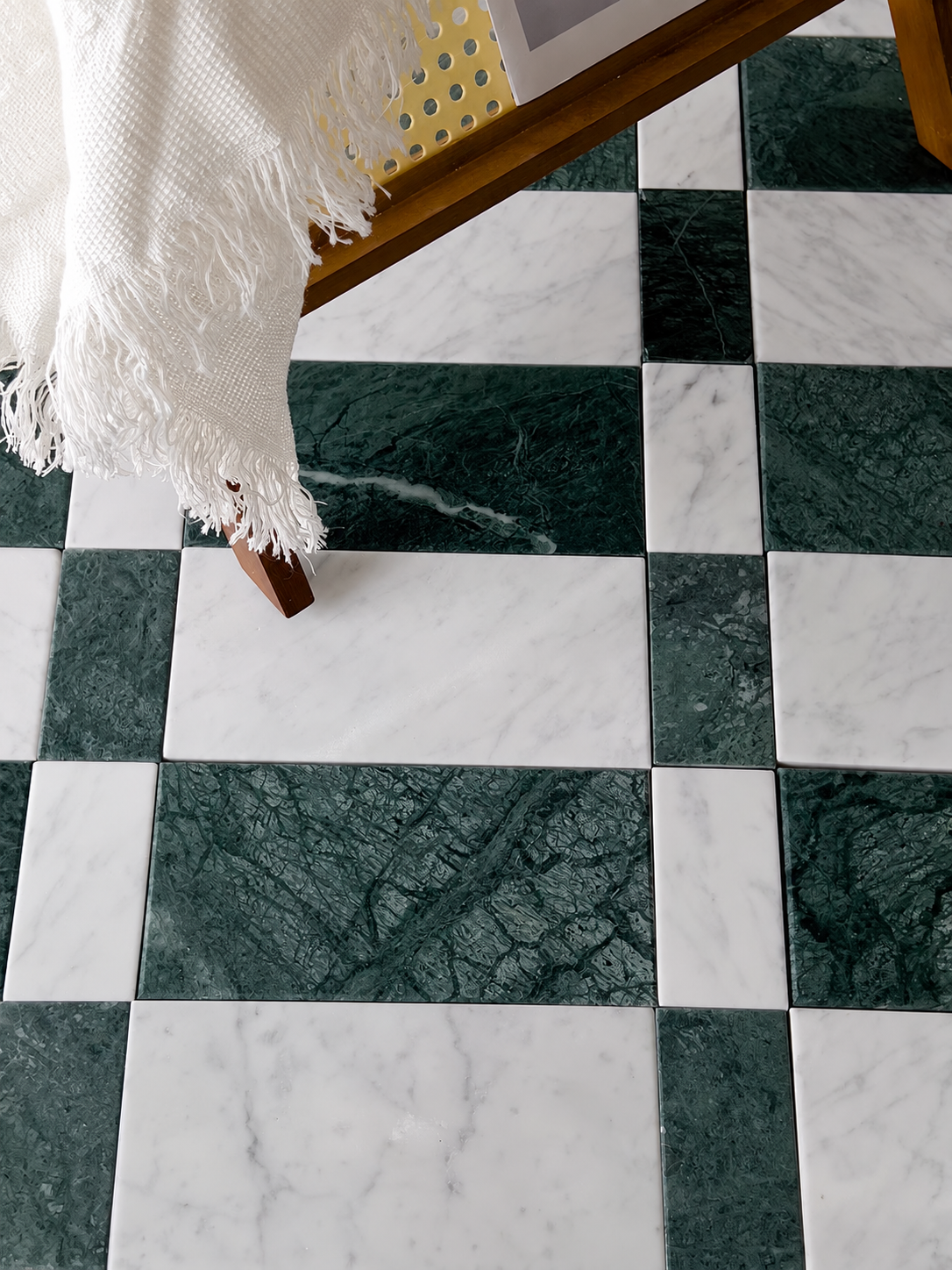Checkered marble floor tiles in dark green and white, with a white fringed throw blanket draped over the edge of a wooden table.