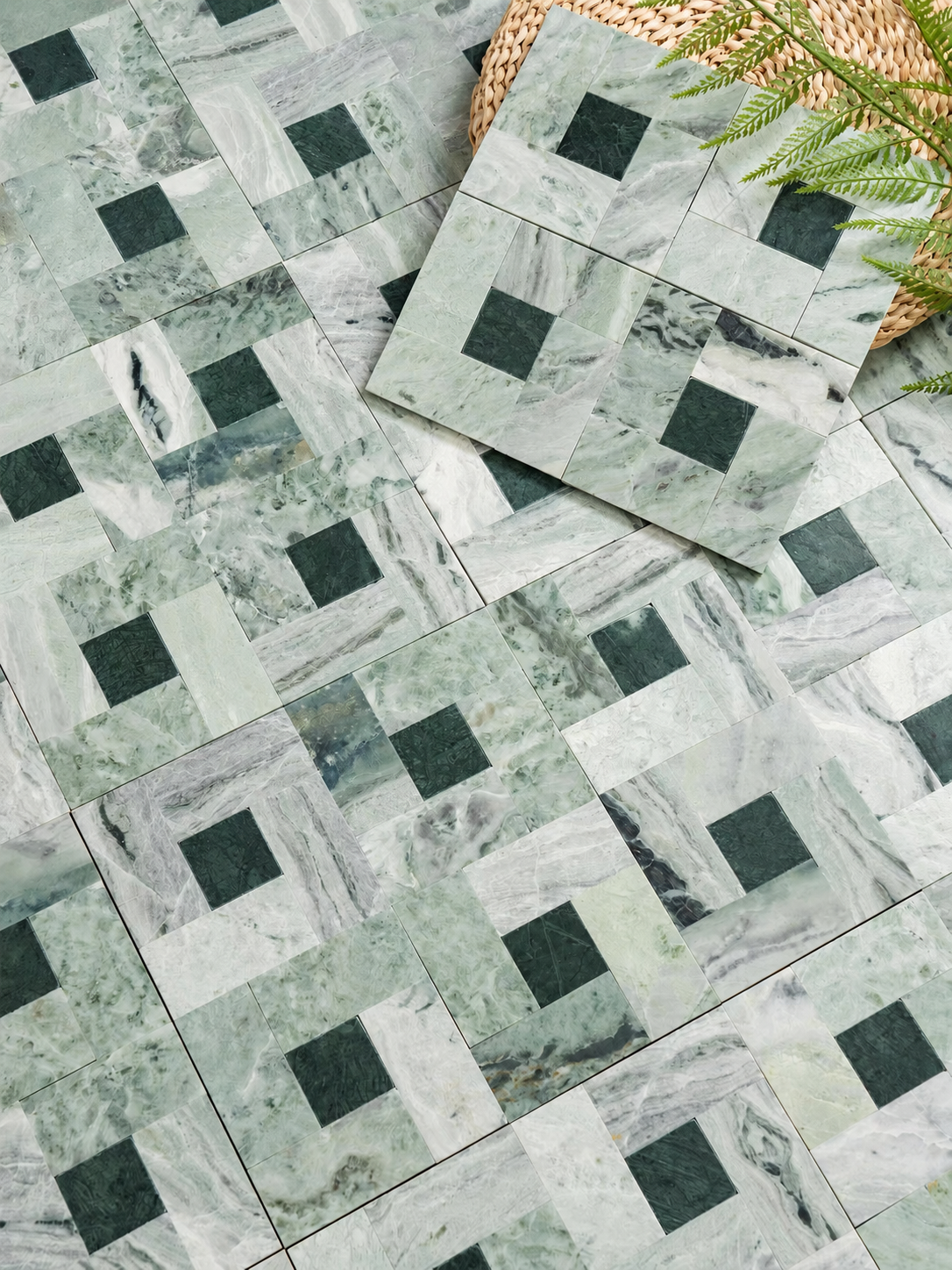 Green marble tiles arranged in a geometric pattern with dark green square inlays, shown with a folded tile and a small woven decorative prop.