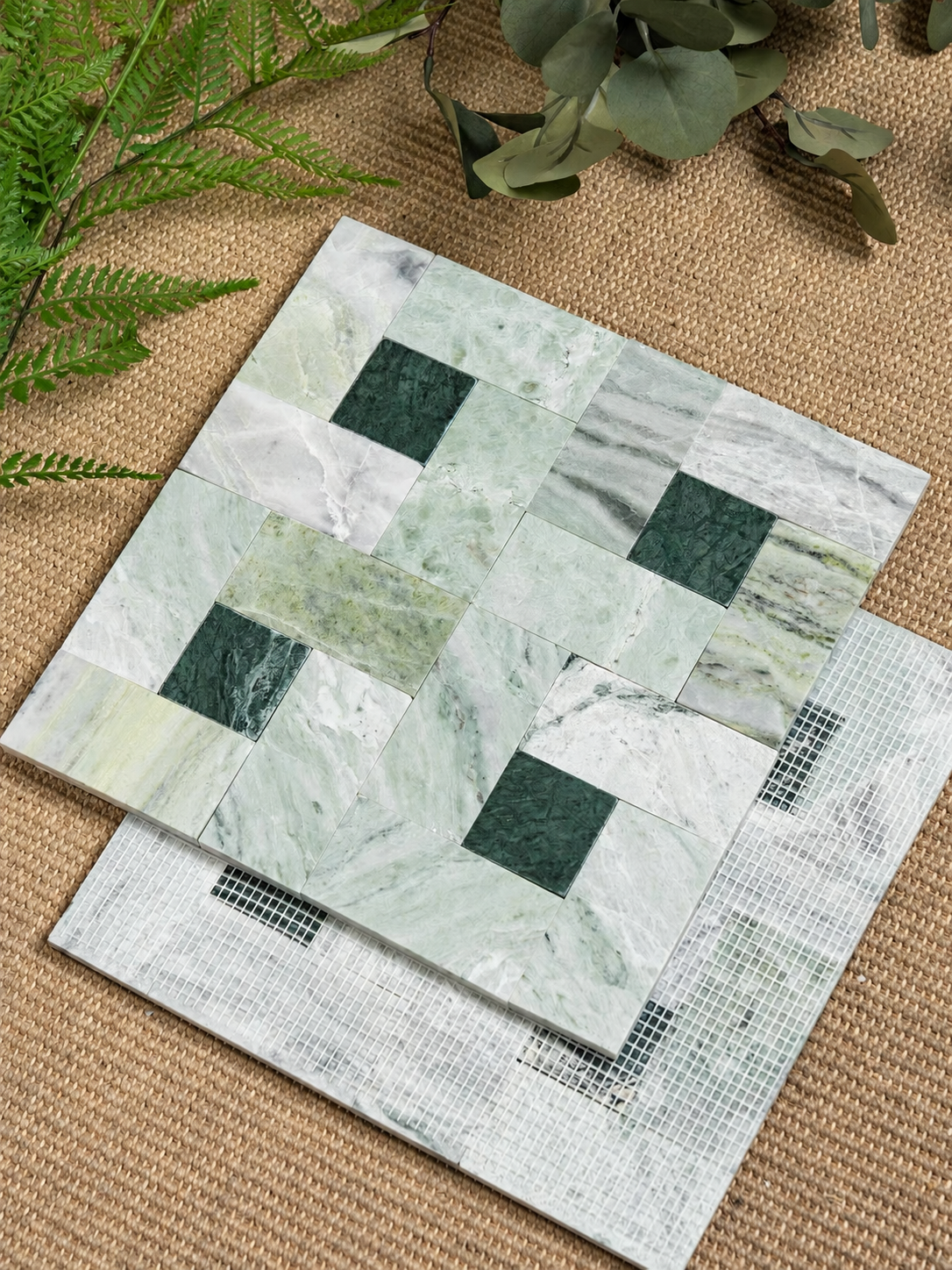 Two square mosaic tiles with a green and white marble pattern, displayed on a burlap background with decorative greenery.