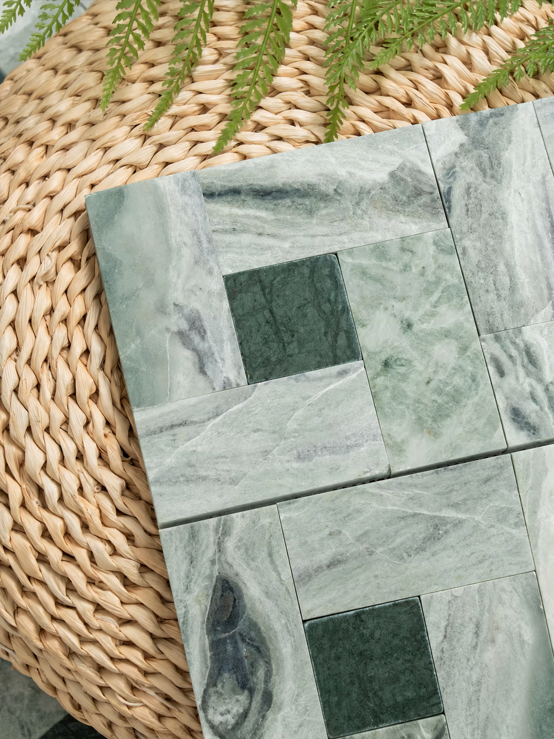 Green marble mosaic wall tiles arranged on a woven straw mat with green foliage at the top.