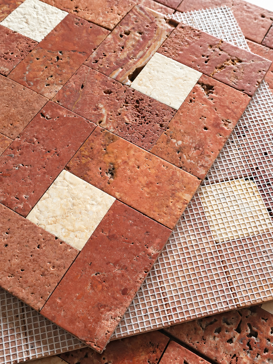 Terracotta and beige stone mosaic tiles arranged on a white mesh background, showing textured brick-like surfaces with natural variation.