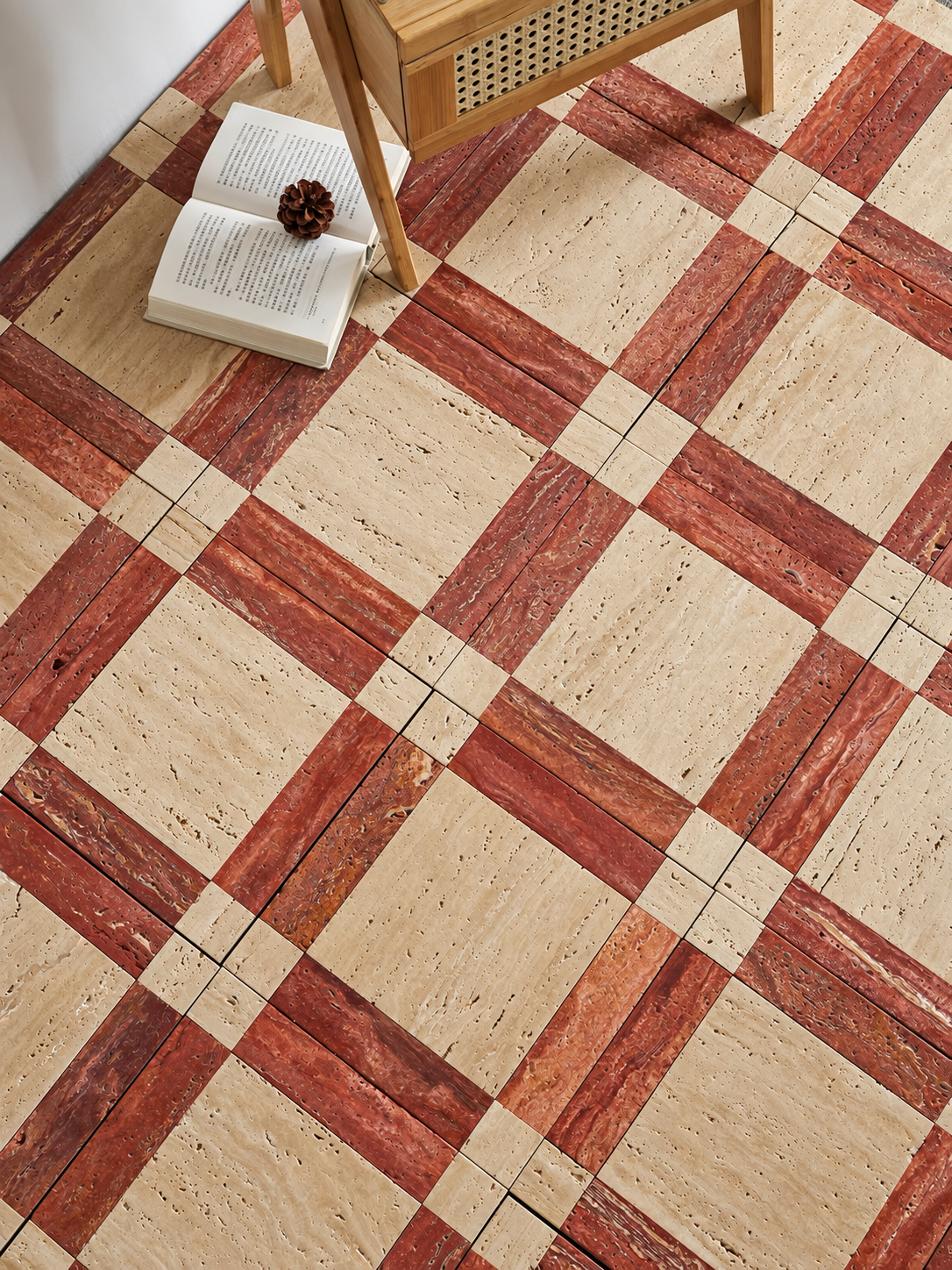 Checkered travertine tile floor in warm beige and reddish-brown tones, styled with an open book, a small pinecone, and part of a wooden chair in the corner.