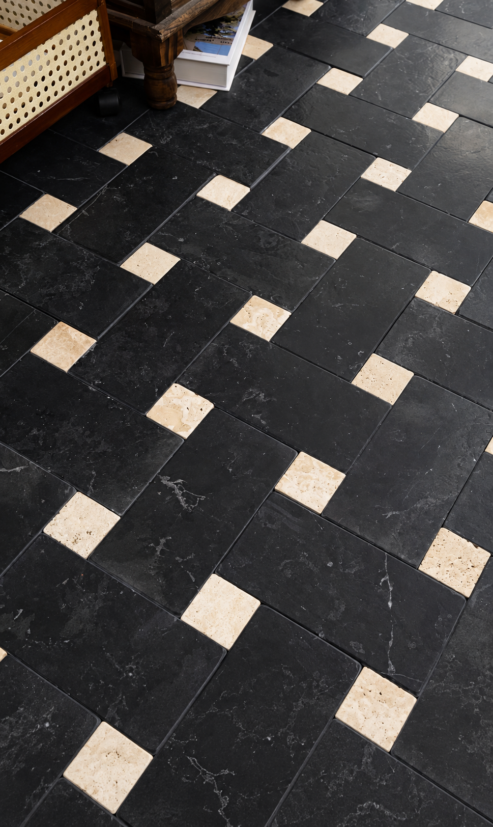 Black stone floor tiles arranged in a geometric pattern with alternating light beige stone squares, shown in a room setting with part of a wooden furniture leg visible in the top left.