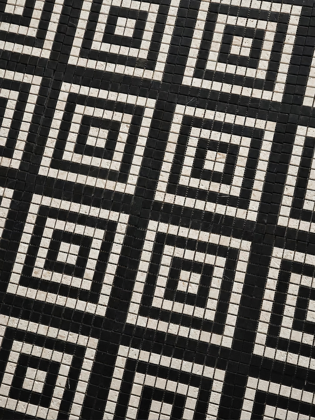 Black and white geometric mosaic tile pattern with repeating concentric square motifs.