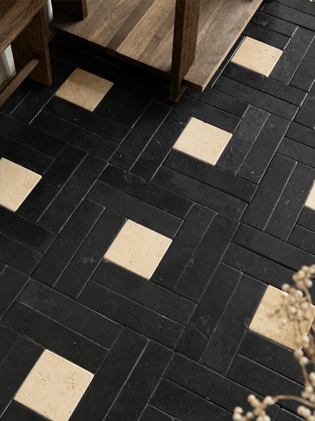 Black rectangular floor tiles arranged in a herringbone pattern with alternating light beige square inlay tiles, shown in a styled interior setting with wooden furniture legs visible.